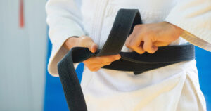 Close-up of a person's hands tying a black belt around their waist