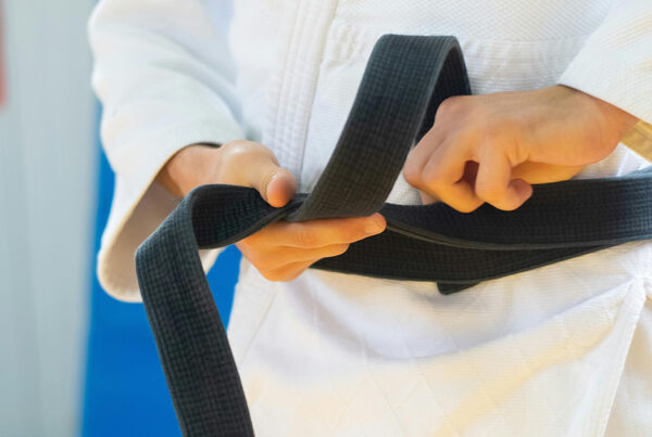 Close-up of a person's hands tying a black belt around their waist