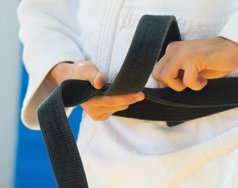 Close-up of a person's hands tying a black belt around their waist