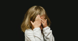 Girl holding her hands to her face against a black background