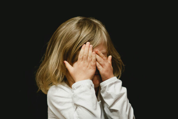 Girl holding her hands to her face against a black background