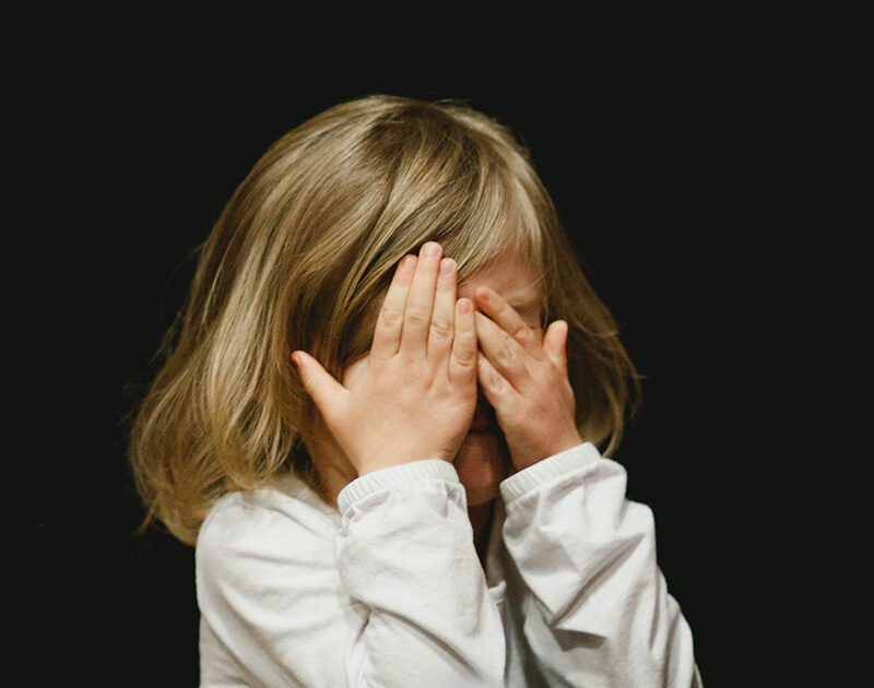 Girl holding her hands to her face against a black background